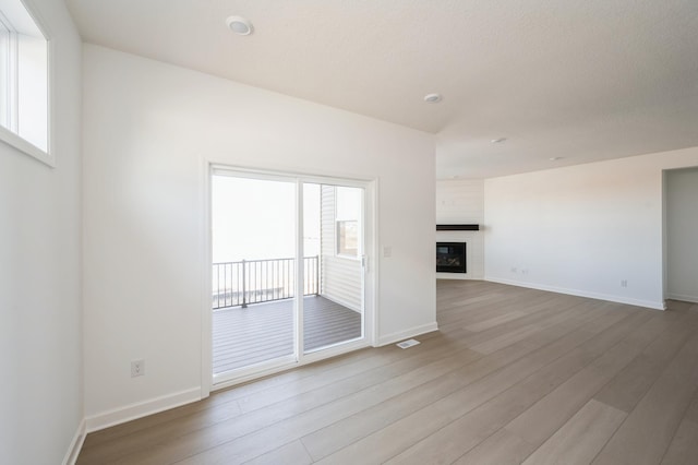 unfurnished living room featuring light wood-type flooring, a glass covered fireplace, visible vents, and baseboards