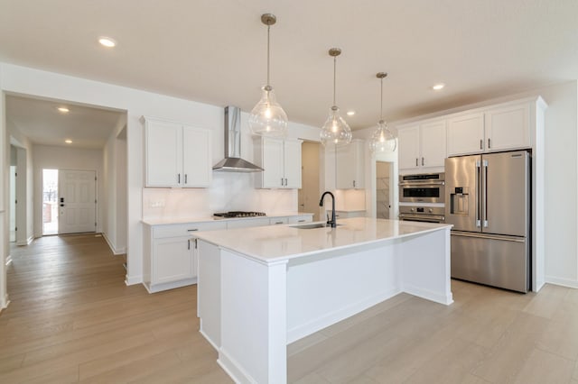 kitchen featuring light countertops, appliances with stainless steel finishes, white cabinets, a sink, and wall chimney exhaust hood