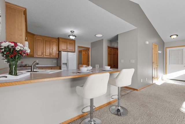 kitchen featuring brown cabinets, a sink, white fridge with ice dispenser, a peninsula, and light colored carpet