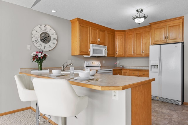 kitchen with a breakfast bar area, light countertops, a peninsula, white appliances, and a textured ceiling