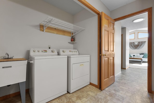 laundry area with baseboards, laundry area, separate washer and dryer, a sink, and stone finish flooring