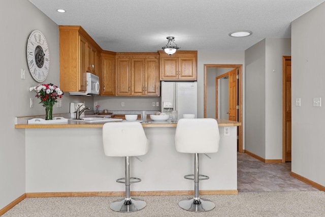 kitchen featuring white appliances, baseboards, a peninsula, a sink, and light countertops