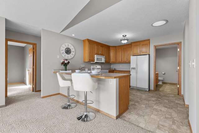 kitchen with baseboards, a kitchen bar, a peninsula, white appliances, and a textured ceiling