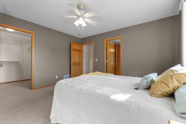 carpeted bedroom featuring a closet, baseboards, a walk in closet, and a ceiling fan