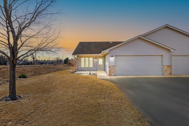 view of front of home with aphalt driveway, an attached garage, a front lawn, and roof with shingles