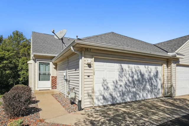 view of side of property with an attached garage, driveway, and roof with shingles