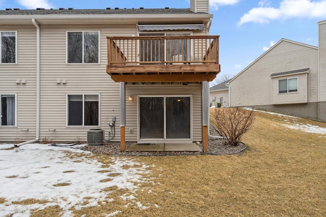 snow covered back of property featuring a yard, a chimney, cooling unit, and a balcony