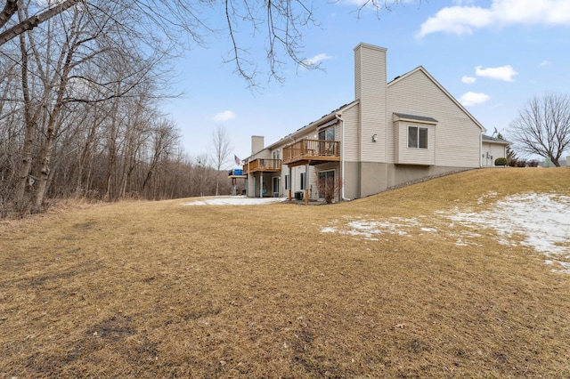 rear view of house with a chimney, a wooden deck, and a lawn