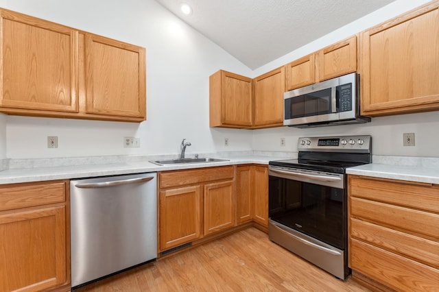 kitchen with light wood-style flooring, appliances with stainless steel finishes, vaulted ceiling, light countertops, and a sink