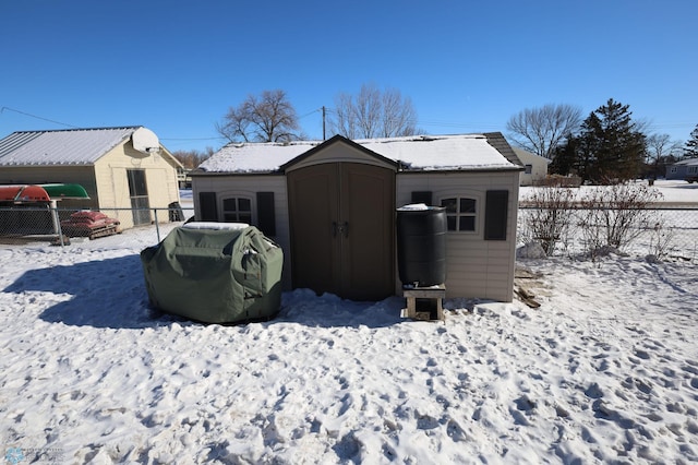 snow covered structure featuring a shed, fence, and an outbuilding