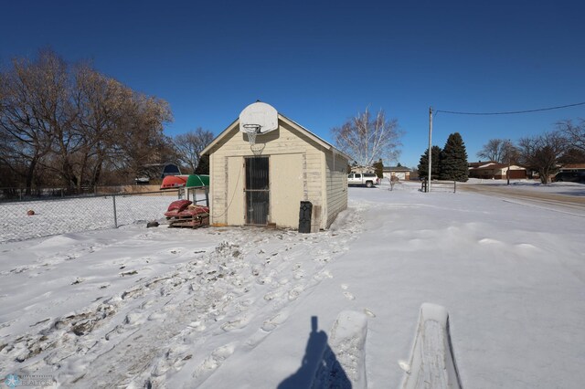 snow covered structure with an outdoor structure, fence, and a storage unit