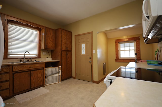 kitchen with white appliances, a sink, baseboards, light countertops, and brown cabinetry