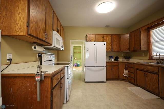 kitchen featuring brown cabinets, light floors, light countertops, a sink, and white appliances