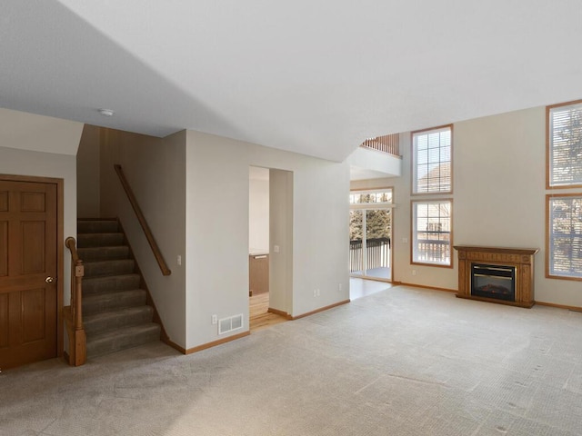 unfurnished living room with light carpet, stairway, and plenty of natural light