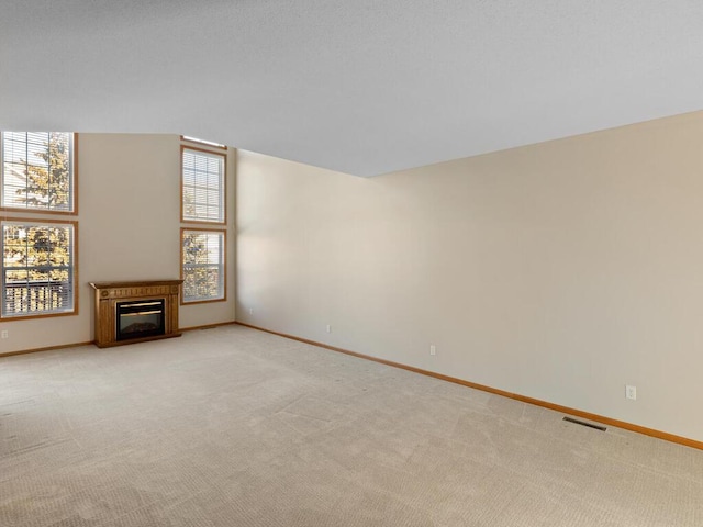 unfurnished living room with light colored carpet, visible vents, a glass covered fireplace, and baseboards