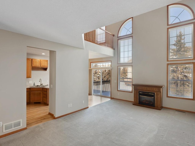 unfurnished living room with light colored carpet, visible vents, a sink, and a glass covered fireplace