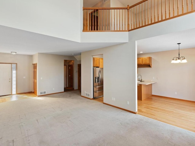 unfurnished living room with light carpet, a notable chandelier, a sink, and baseboards