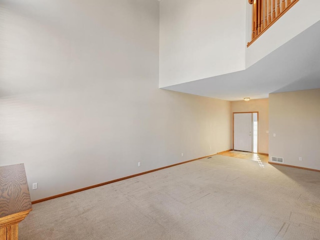 empty room featuring a towering ceiling, visible vents, light carpet, and baseboards