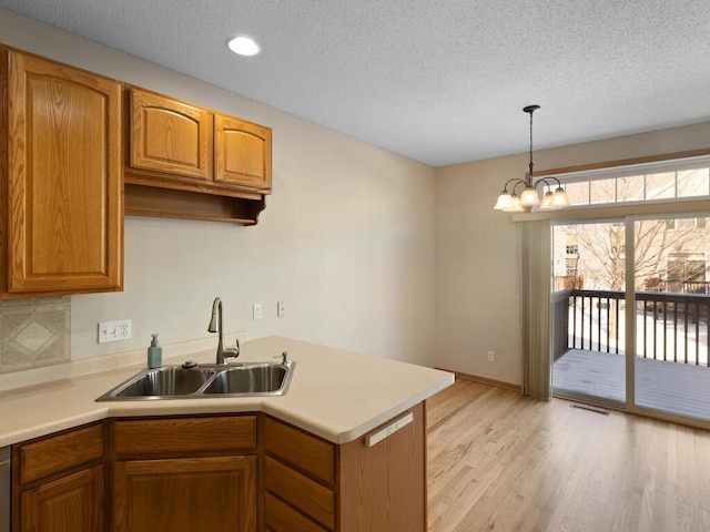 kitchen featuring brown cabinetry, hanging light fixtures, light countertops, light wood-type flooring, and a sink