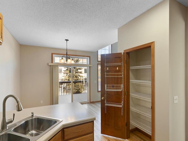 kitchen featuring an inviting chandelier, light countertops, light wood-type flooring, pendant lighting, and a sink