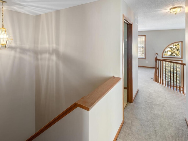 hallway featuring light carpet, a textured ceiling, an upstairs landing, and baseboards