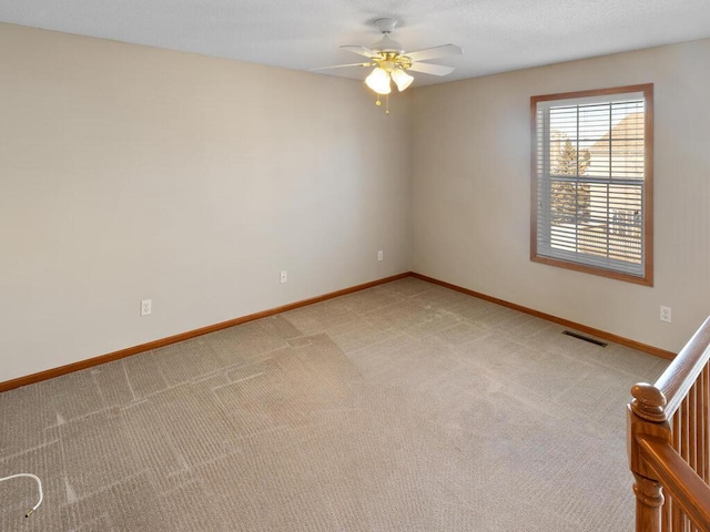 spare room featuring a ceiling fan, light colored carpet, visible vents, and baseboards