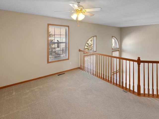 spare room with light carpet, baseboards, visible vents, and a ceiling fan