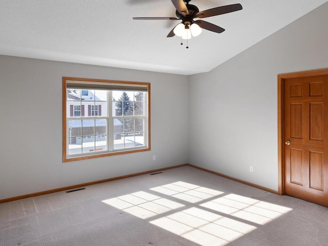 unfurnished room with baseboards, vaulted ceiling, visible vents, and light colored carpet