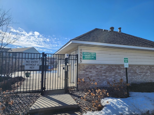 view of property exterior featuring a gate, brick siding, fence, and roof with shingles