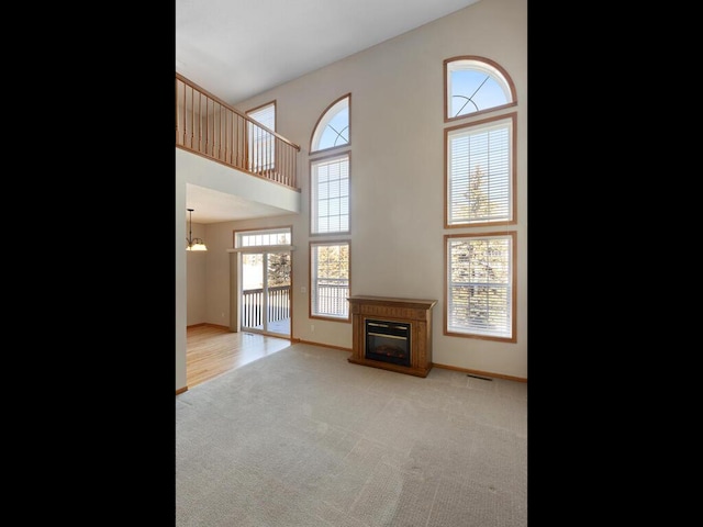 living room with a towering ceiling, baseboards, light colored carpet, and a glass covered fireplace