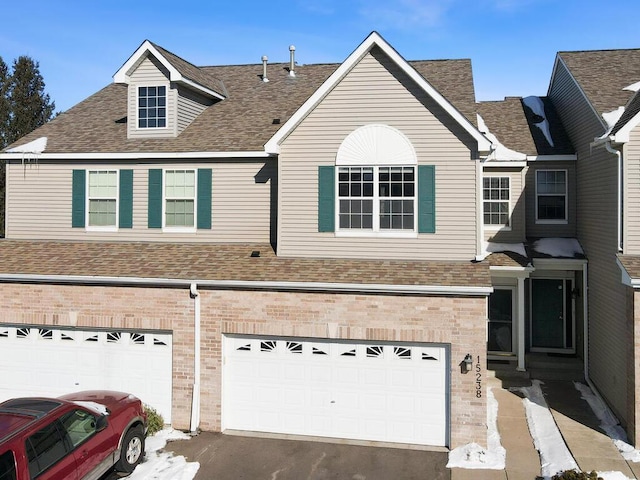 view of property featuring an attached garage, a shingled roof, and brick siding