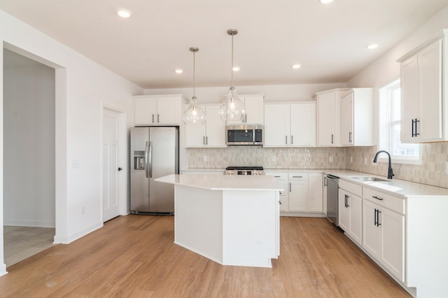 kitchen featuring decorative light fixtures, appliances with stainless steel finishes, white cabinetry, a kitchen island, and a sink