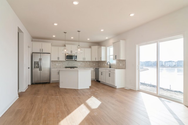 kitchen featuring white cabinets, a kitchen island, appliances with stainless steel finishes, hanging light fixtures, and light countertops