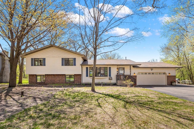 tri-level home featuring an attached garage, asphalt driveway, brick siding, and a front lawn
