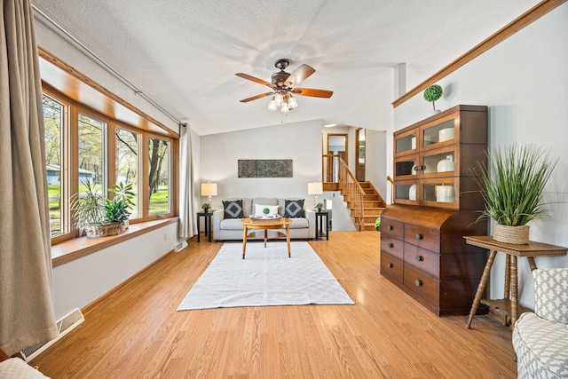 living area featuring vaulted ceiling, light wood finished floors, ceiling fan, stairs, and baseboards