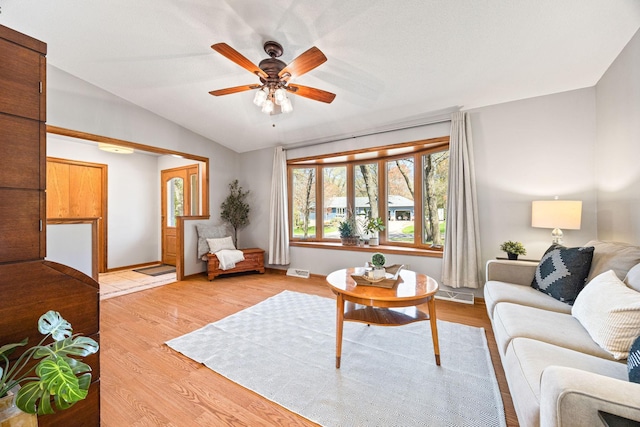 living room featuring light wood-style flooring, vaulted ceiling, ceiling fan, and baseboards