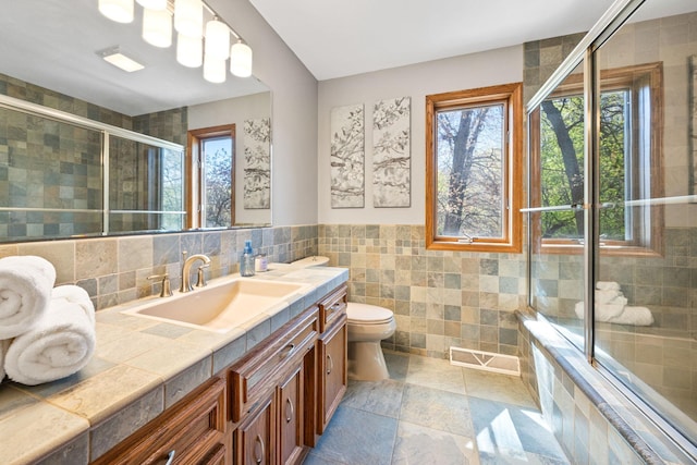 bathroom with tile walls, healthy amount of natural light, tiled shower, vanity, and toilet