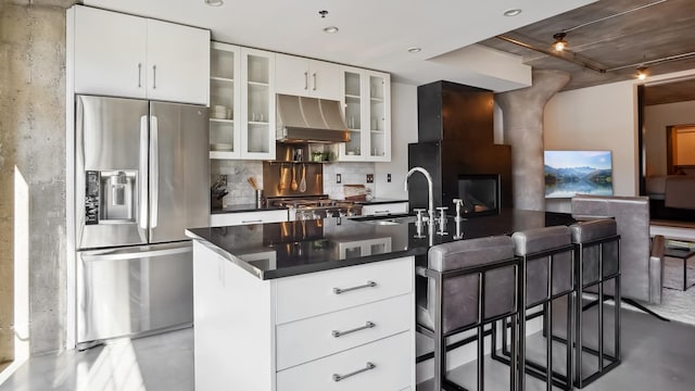 kitchen with dark countertops, ventilation hood, a kitchen bar, stainless steel refrigerator with ice dispenser, and a sink