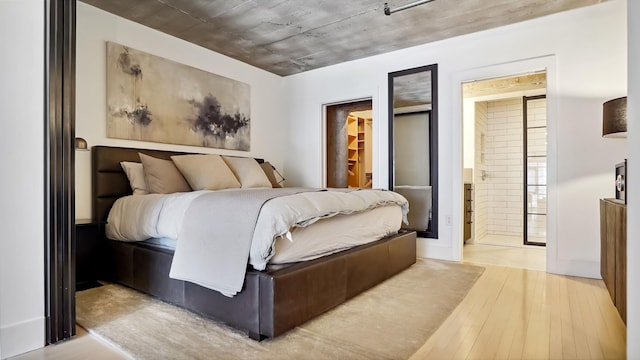 bedroom with a walk in closet, wood finished floors, and ensuite bathroom