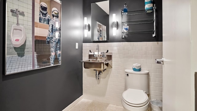 bathroom featuring tile patterned flooring, toilet, a wainscoted wall, a sink, and tile walls