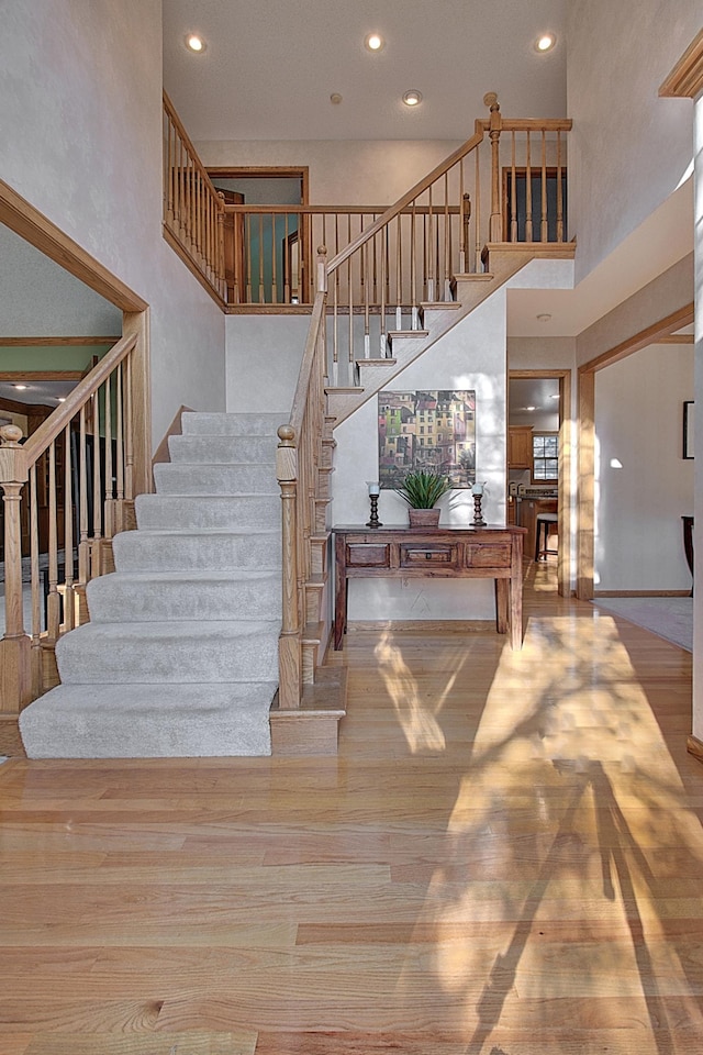 stairs featuring a towering ceiling, wood finished floors, and recessed lighting