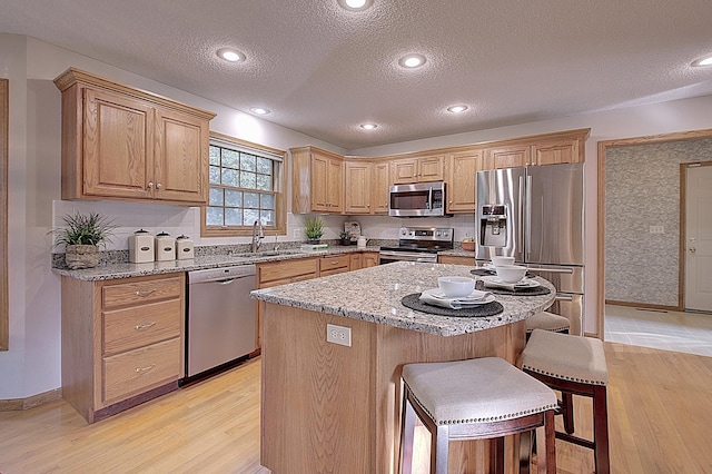 kitchen featuring light stone counters, a breakfast bar area, stainless steel appliances, a sink, and a kitchen island