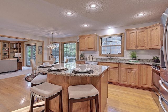 kitchen with light stone counters, a center island, decorative light fixtures, light wood-type flooring, and a sink