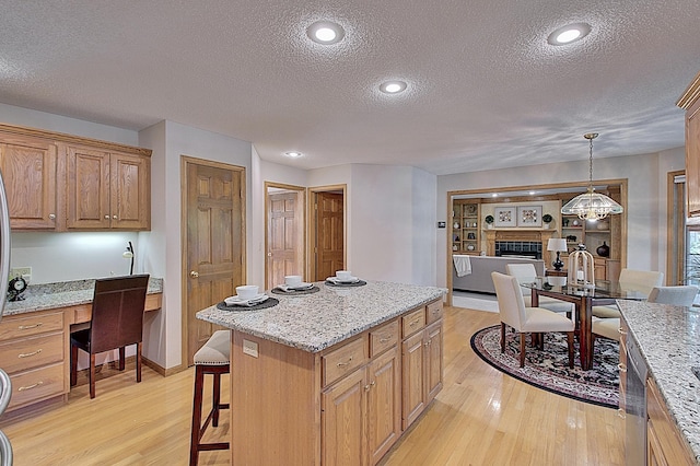 kitchen with light wood finished floors, built in desk, a kitchen island, and light stone counters