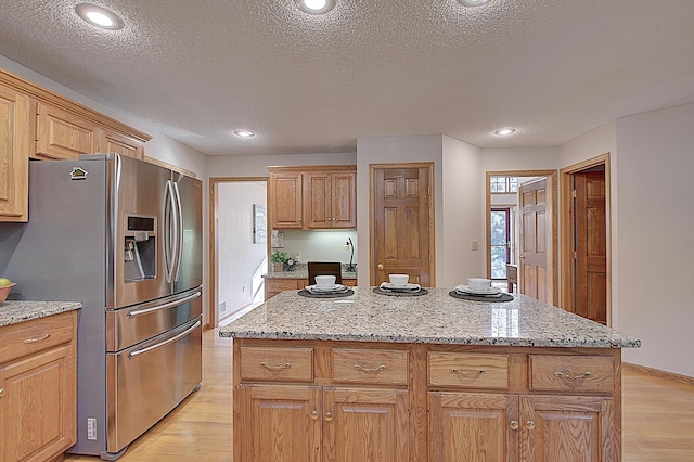 kitchen featuring light stone countertops, light wood finished floors, a kitchen island, and stainless steel fridge with ice dispenser