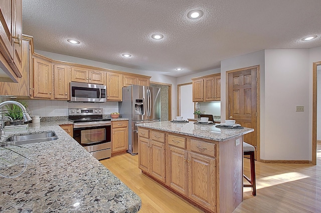 kitchen with a sink, a kitchen island, light wood-style floors, appliances with stainless steel finishes, and light stone countertops