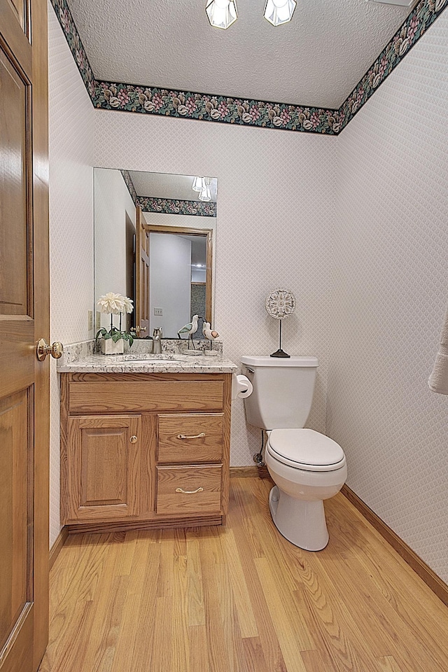 half bathroom featuring toilet, wallpapered walls, a textured ceiling, and wood finished floors