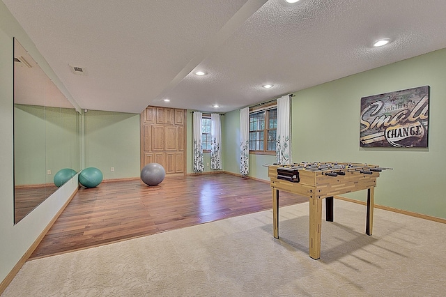 recreation room featuring visible vents, light colored carpet, a textured ceiling, and baseboards