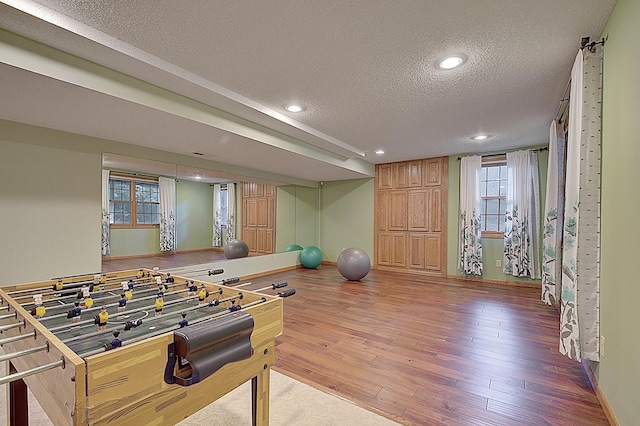 recreation room featuring a textured ceiling, light wood finished floors, baseboards, and recessed lighting