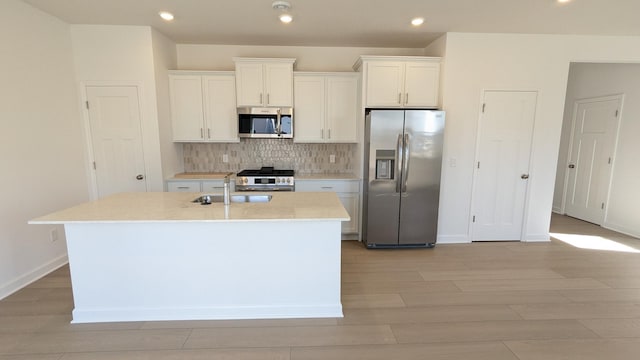 kitchen featuring stainless steel appliances, an island with sink, decorative backsplash, and white cabinetry